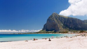 Une plage avec une grande montagne en arrière-plan, une eau d’un bleu limpide et des gens qui se détendent sur le sable.