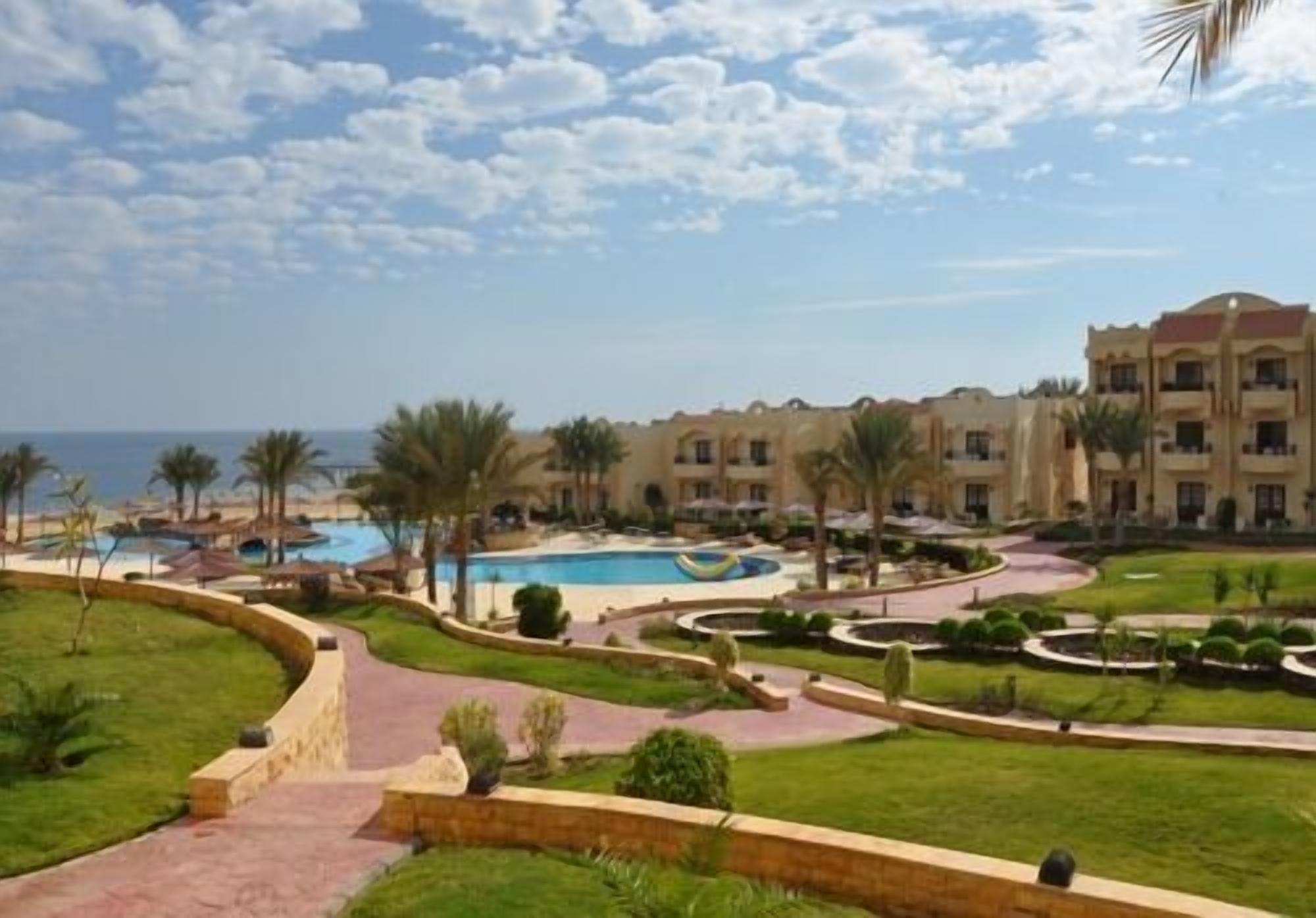 A resort with a swimming pool, palm trees, and a view of the sea.