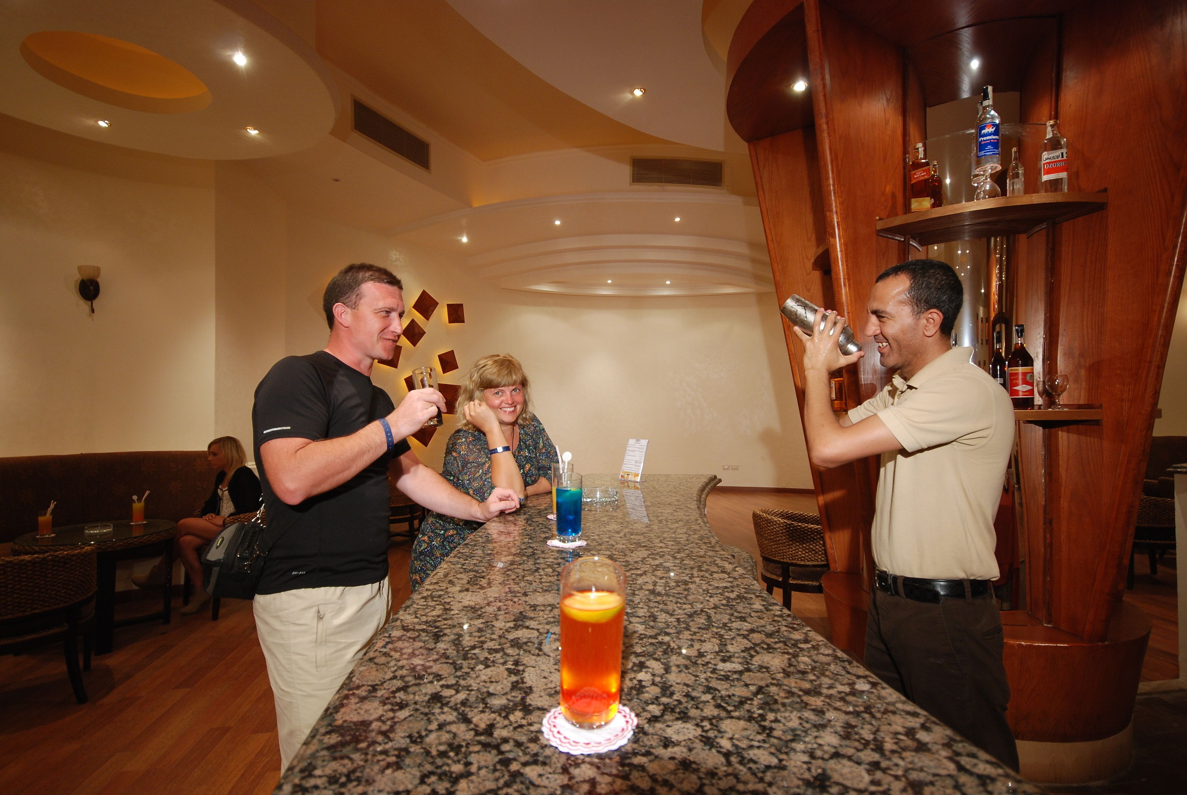 A bar area with a granite countertop, a barista preparing a drink, and a customer receiving it.