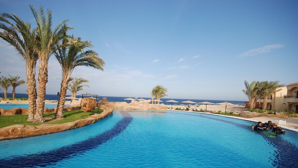 A swimming pool with palm trees and a view of the sea. - Life Resort Coral Hills - All inclusive (El Quseir)