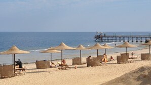 A beach with thatched umbrellas and wooden benches, a pier in the background, and a calm sea. - Life Resort Coral Hills - All inclusive (El Quseir)