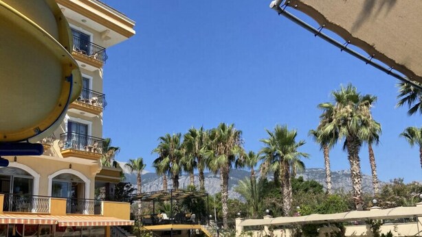 A swimming pool with lounge chairs and umbrellas, a water slide, palm trees, and a building with balconies. - Stella Hotel (Kemer)