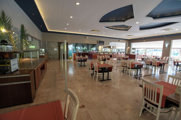 Un restaurante amplio con varias mesas y sillas, una barra con una vitrina y vistas al exterior.