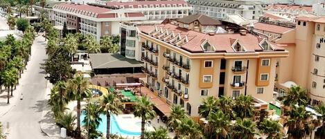 A coastal hotel with a swimming pool, palm trees, and a view of the sea.