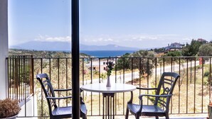 Un balcon avec deux chaises et une table, offrant une vue panoramique sur un paysage magnifique, avec des montagnes et une étendue d’eau.