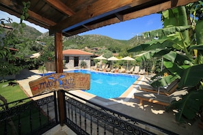 Zona de piscina con sillas de descanso y sombrillas, rodeada de vegetación y un paisaje montañoso.