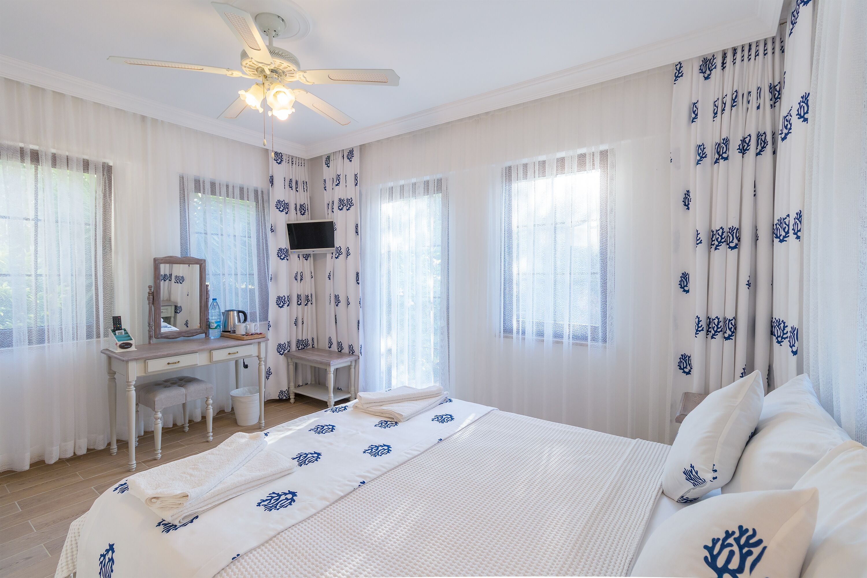 Un dormitorio con cama, escritorio, silla, espejo y ventilador de techo.