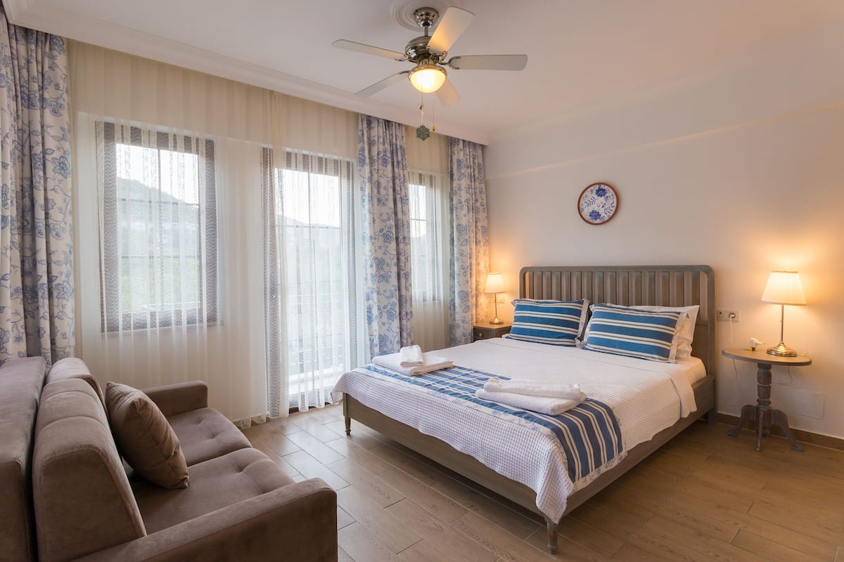Een hotelkamer met een bed, een sofa, een plafondventilator en twee bedlampen.