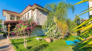 Una casa con jardín cuidado, que incluye césped, una piscina pequeña y diversas plantas.