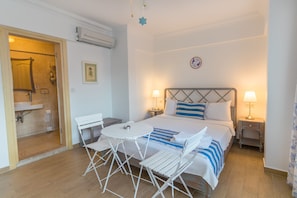Un dormitorio con cama, dos mesitas de noche, una mesilla, una pequeña mesa con sillas y un baño visible a través de una puerta abierta.