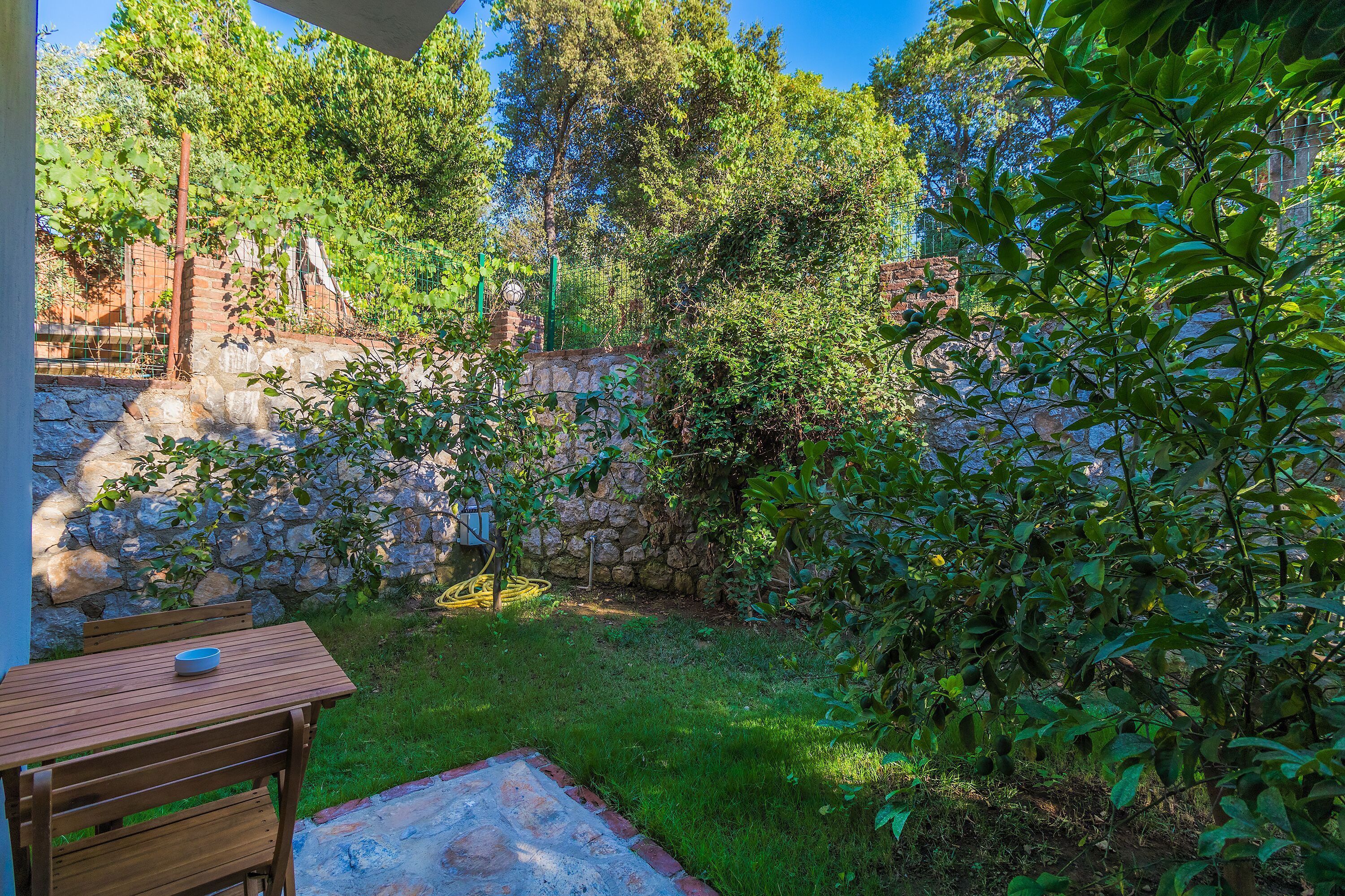 A garden with a stone wall, a wooden table, and a bench.