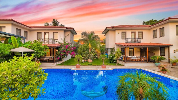 Una piscina rodeada de casas de dos pisos con balcones, un patio cubierto y abundante vegetación.