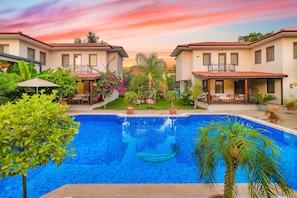 Une piscine entourée de maisons à deux étages dotées de balcons, d’un patio couvert et d’une végétation luxuriante.