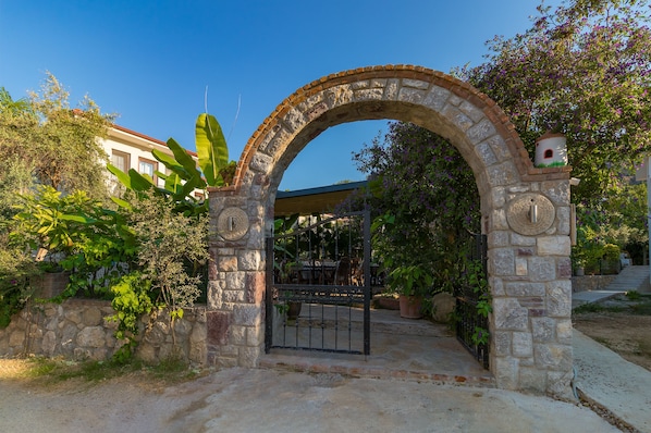 Un arco de entrada a un espacio al aire libre cubierto, con pared de piedra y plantas en macetas.