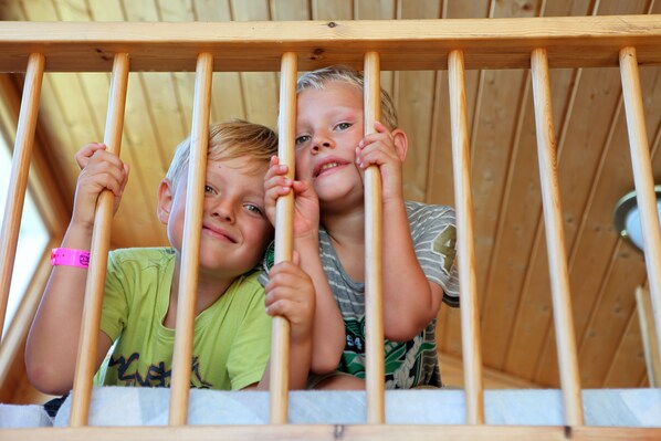 Two children leaning on wooden bars in a room with a wooden ceiling.