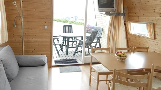 Una cabaña de madera con sofá, mesa de comedor, sillas y televisor.