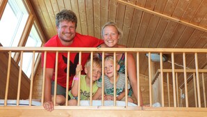 Una familia en una terraza de madera con barandilla, paredes de madera y techo inclinado.