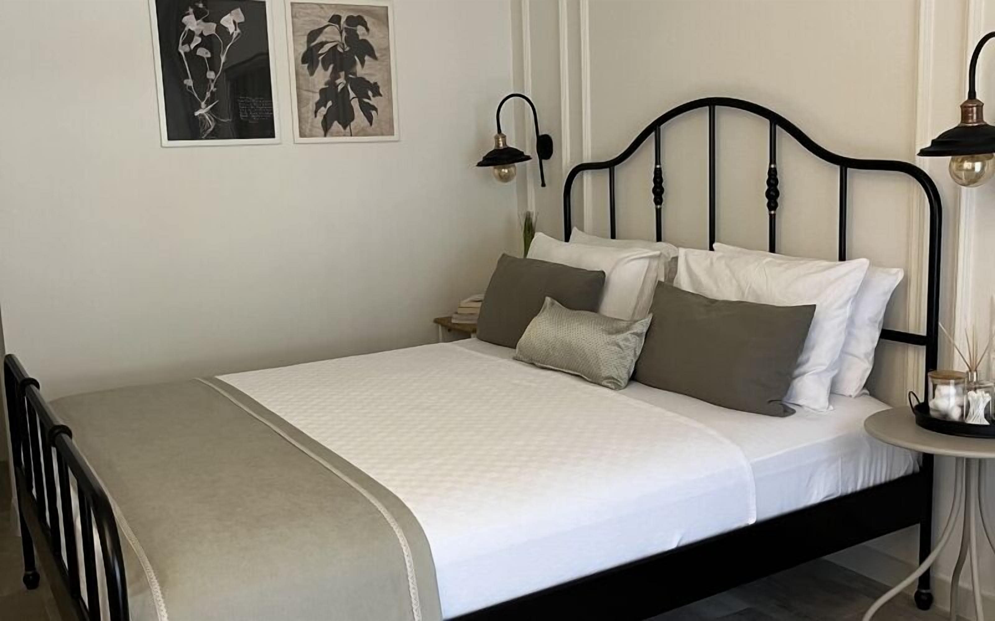 A neatly made bed with white bedding and multiple pillows, a bedside table with a lamp, and two framed pictures on the wall.