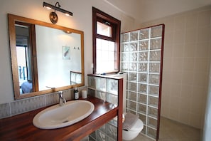 A bathroom with a wooden vanity, a large mirror, a glass shower enclosure, and a white toilet.