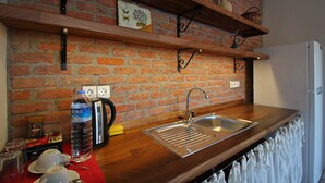 Une cuisine avec un mur en briques, des étagères en bois, un évier en acier inoxydable et une bouilloire.