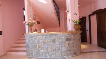 A stone reception desk with a vase of flowers, a clock, and a staircase in the background.