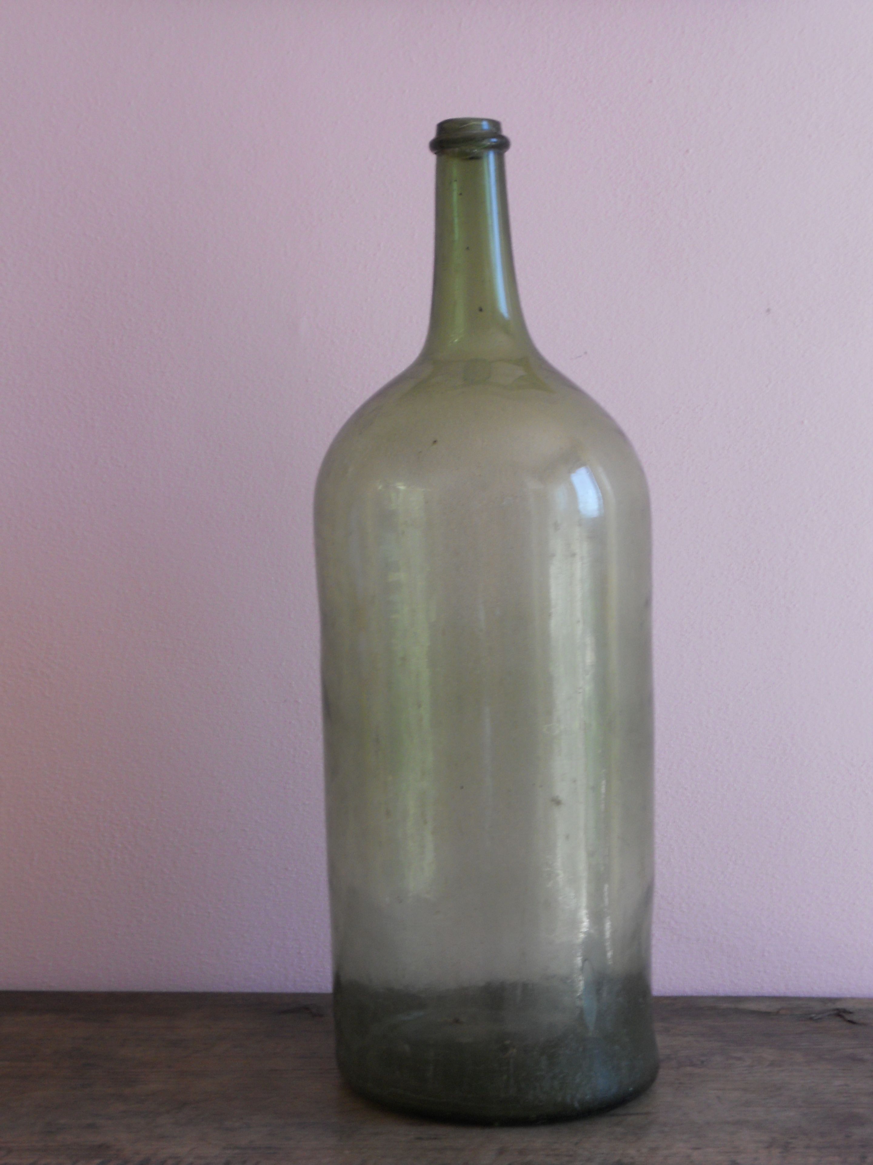 A clear glass bottle with a narrow neck and a wider base, standing upright on a flat surface against a plain background.