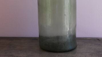 A clear glass bottle with a narrow neck and a wider base, standing upright on a flat surface against a plain background.