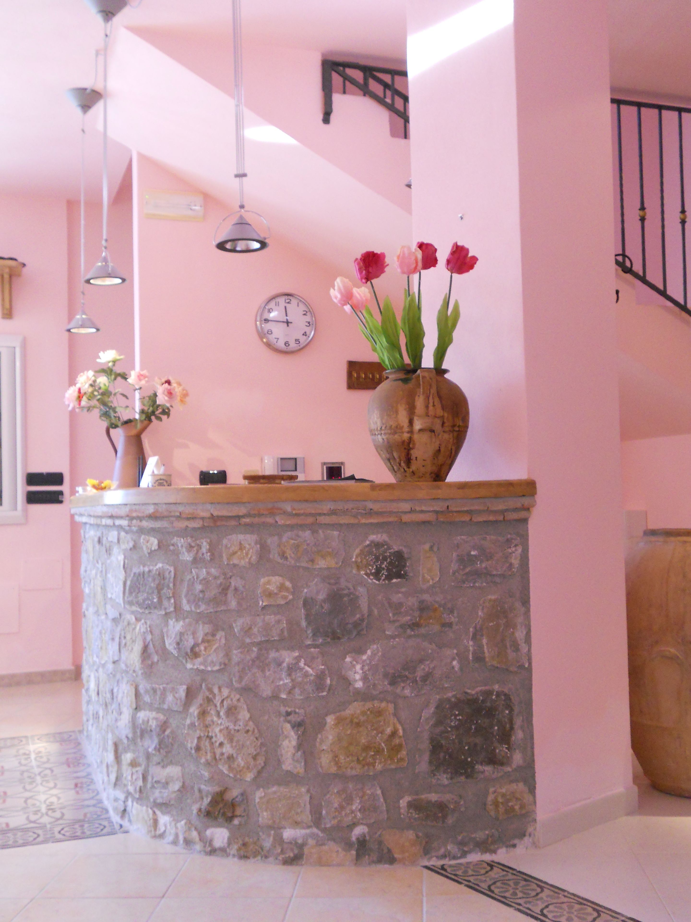 A stone reception desk with a vase of flowers, a clock, and a staircase.