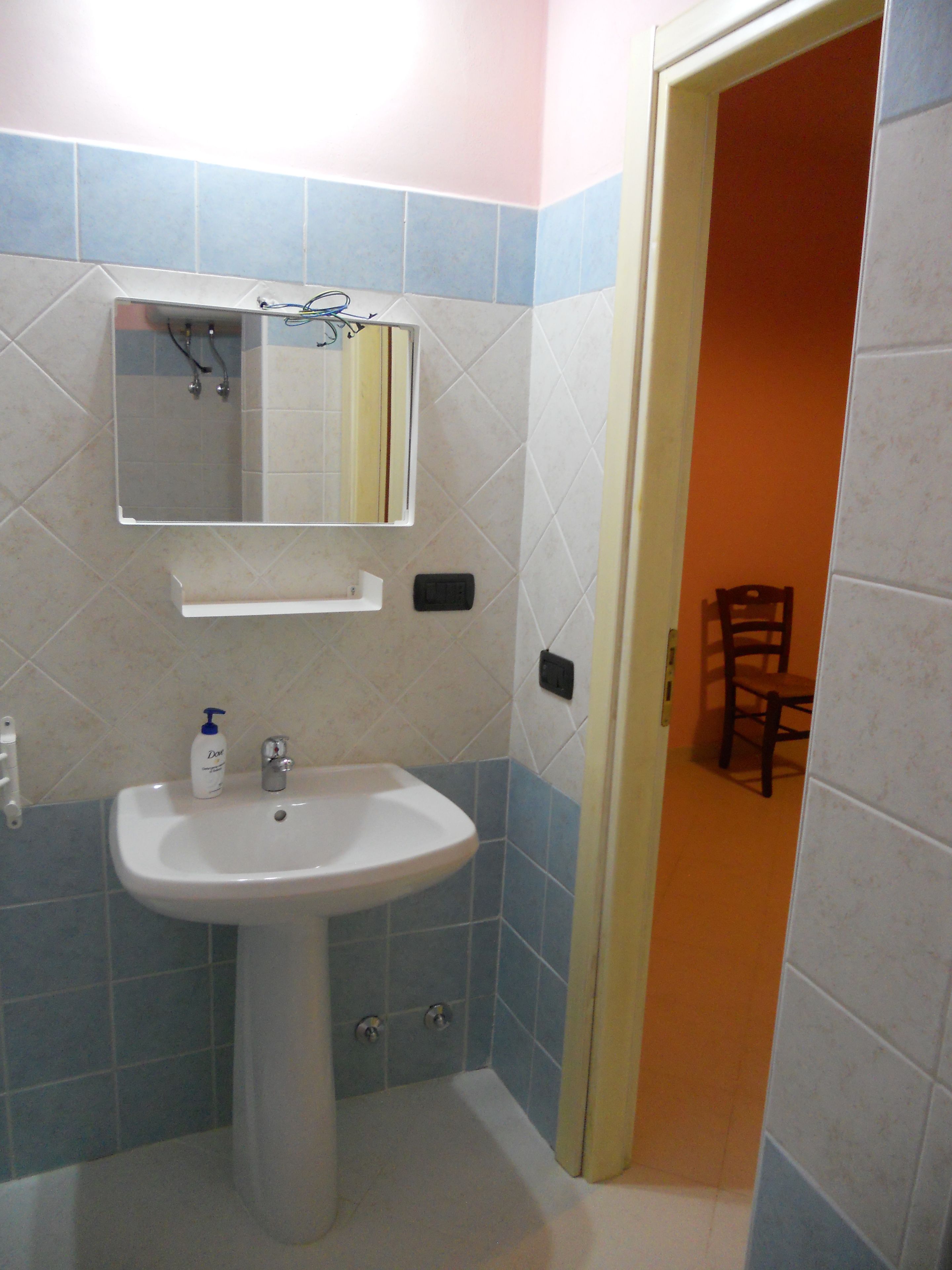 A bathroom with a sink, mirror, and a chair in the background.