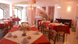 Uma sala de jantar com mesas preparadas para um chá, apresentando xícaras e pires brancos, e um vaso com flores.