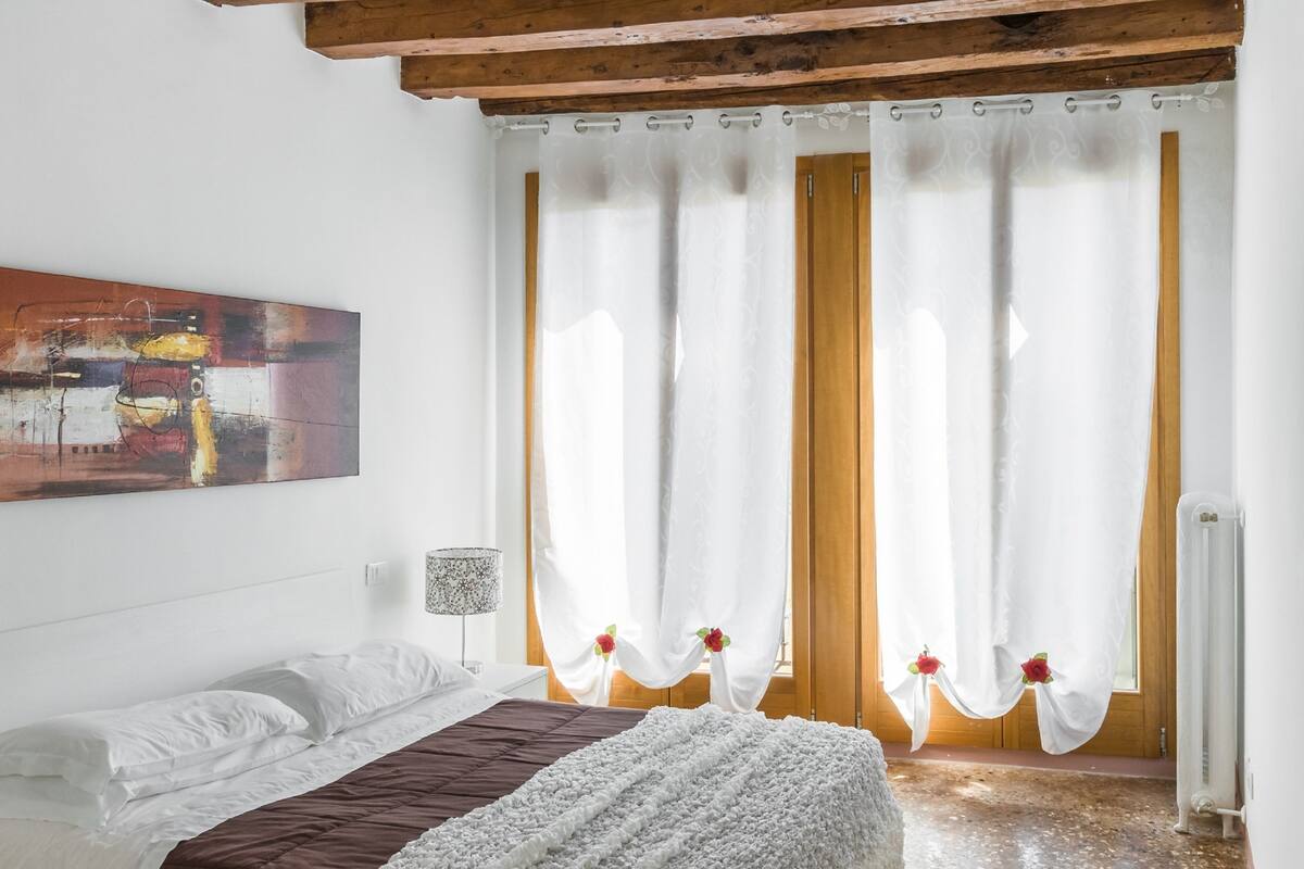 Un dormitorio con cama, un cuadro, una lámpara y cortinas.