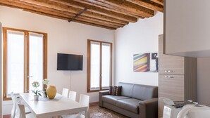 A modern living room with a wooden ceiling, a white dining table with chairs, a grey sofa, and a flat-screen TV mounted on the wall. - Dorsoduro Charme Apartments by Wonderful Italy (Venice)