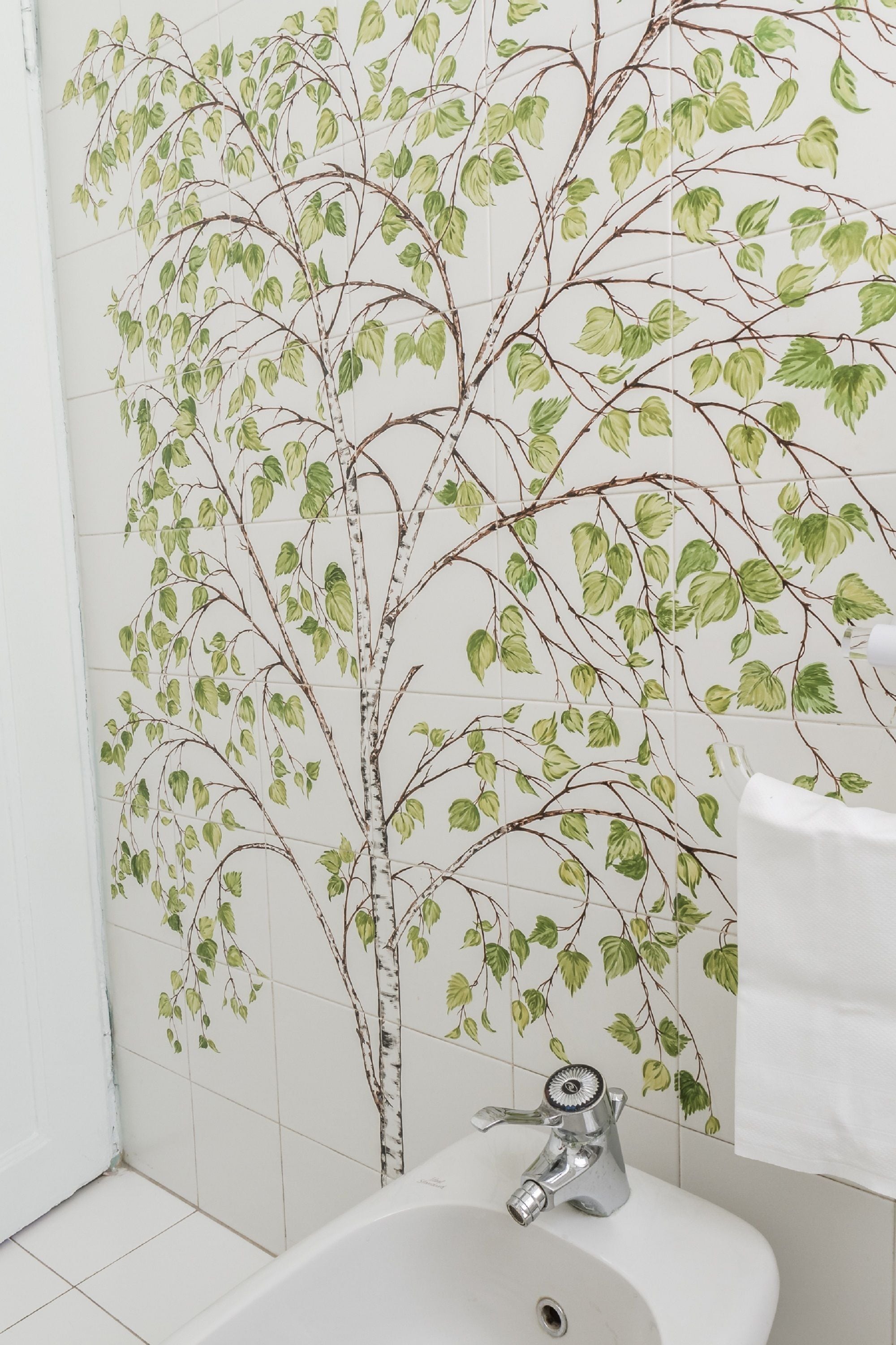 A bathroom with a white sink, a modern faucet, and a wall decorated with a green leafy branch pattern.