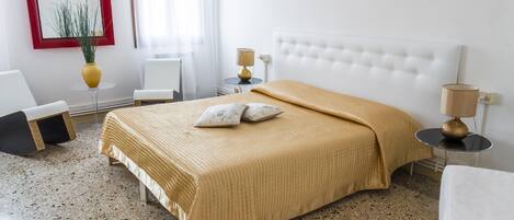 A hotel room with a bed, two bedside tables, a chair, a small table, a lamp, and a mirror on the wall.