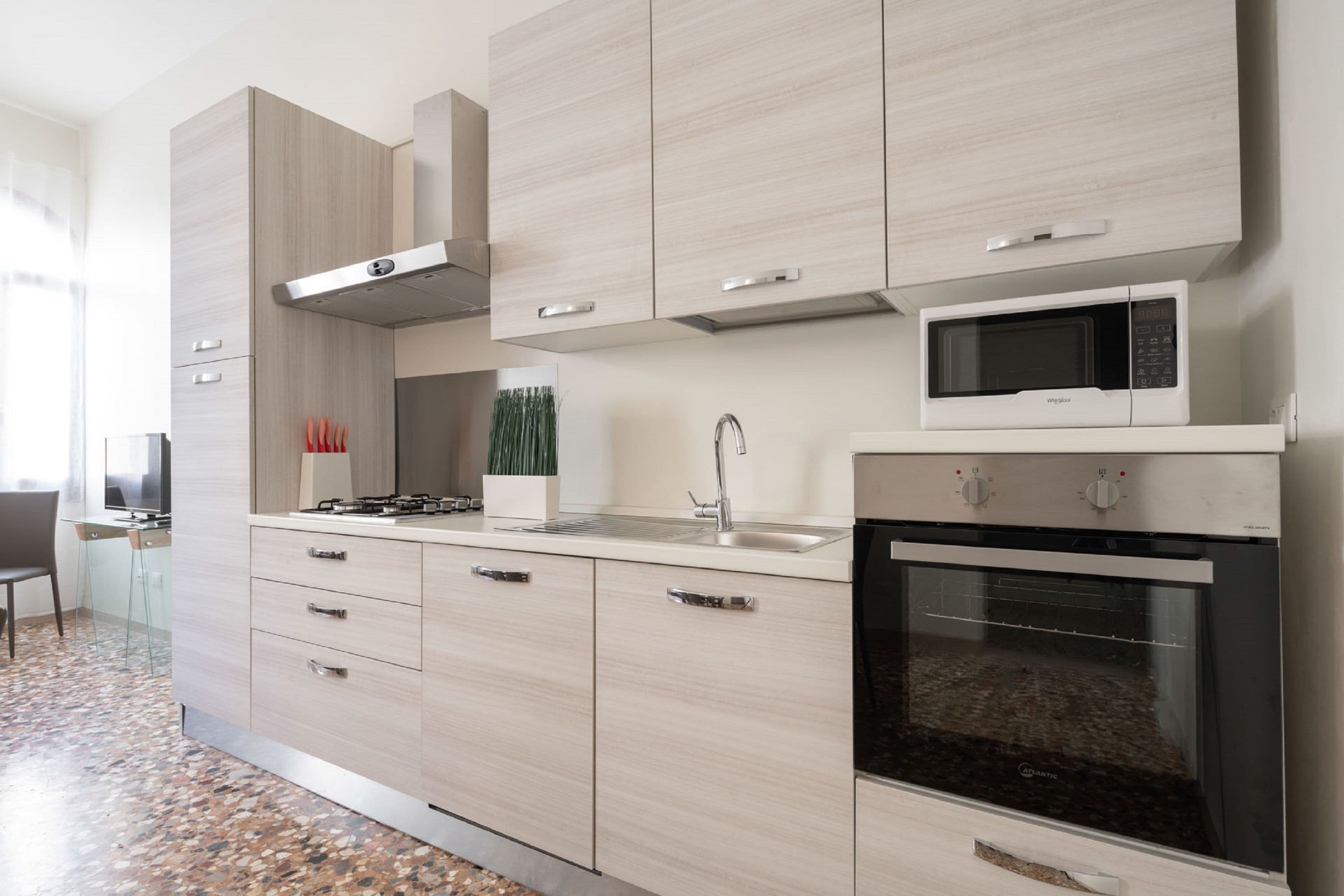 Una cocina moderna con armarios de madera clara, una campana extractora de acero inoxidable, un microondas y un horno empotrado.