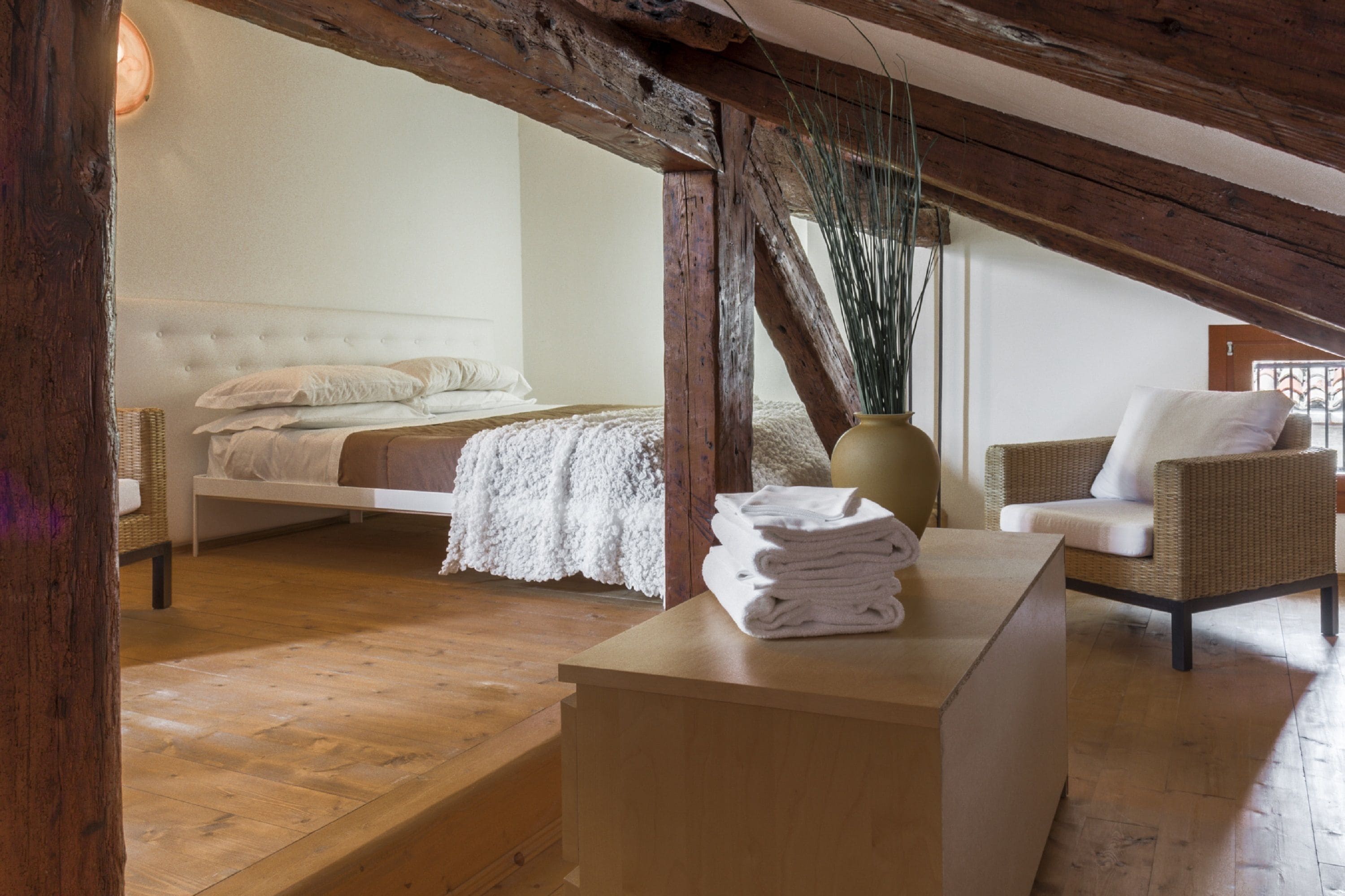 A bedroom with a bed, a chair, a table, and a vase.