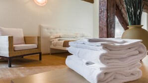 A neatly arranged stack of white towels on a wooden table in a room with a wicker chair and a bed with white bedding. - Dorsoduro Charme Apartments by Wonderful Italy (Venice)