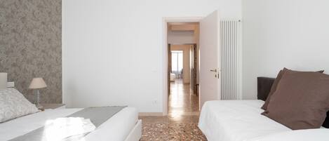 A hotel room with a bed, a nightstand, a lamp, and a door leading to another room.