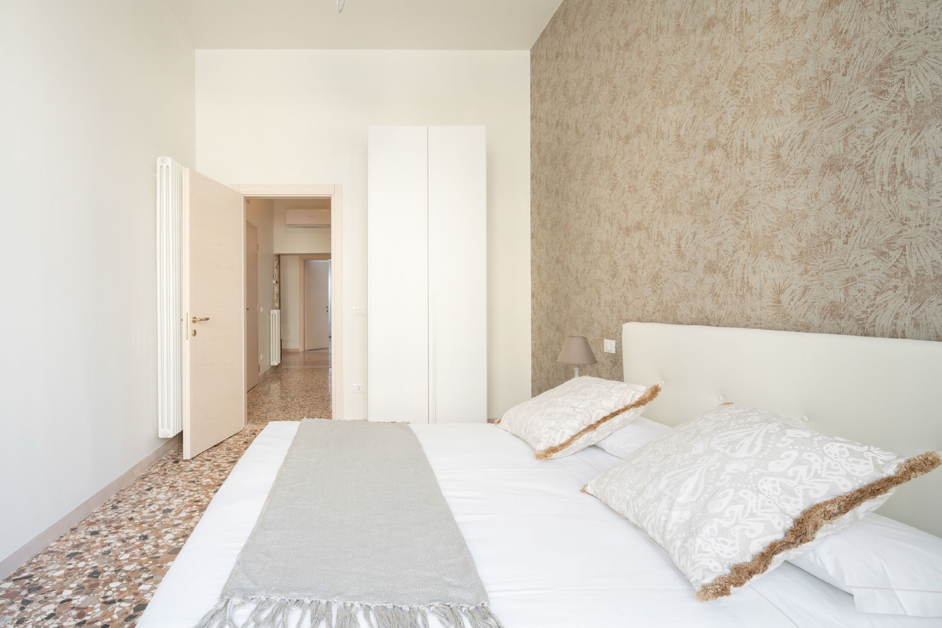 A bedroom with a large bed, a bedside table, a nightstand, and a door leading to another room.