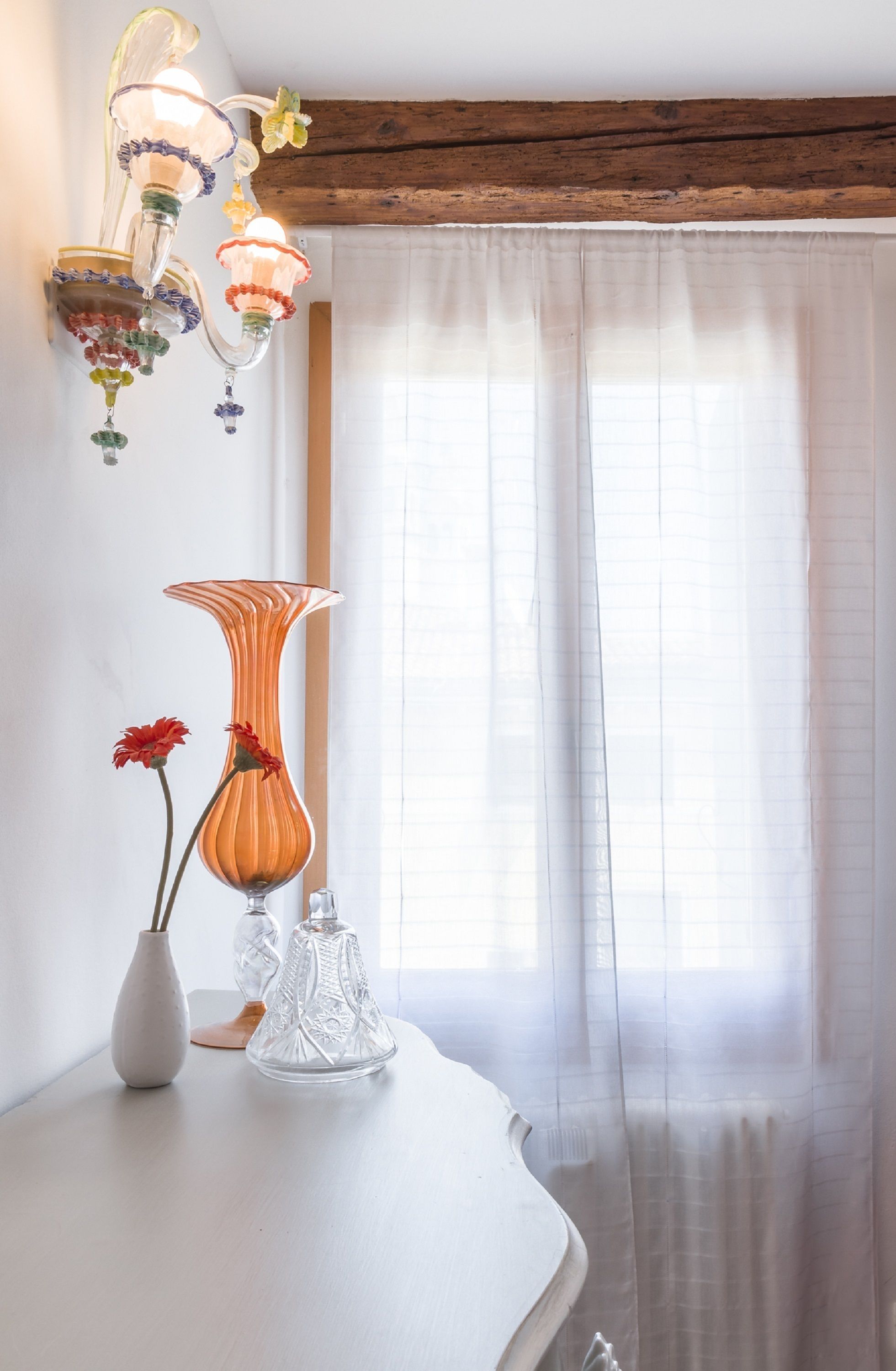 A room with a wooden ceiling, a white table with two vases, one with red flowers, and a clear glass vase.