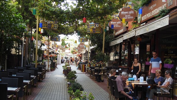 Ein lebhaftes Straßencafé mit Tischen und Stühlen, umgeben von Grünpflanzen und hängenden Dekorationen.