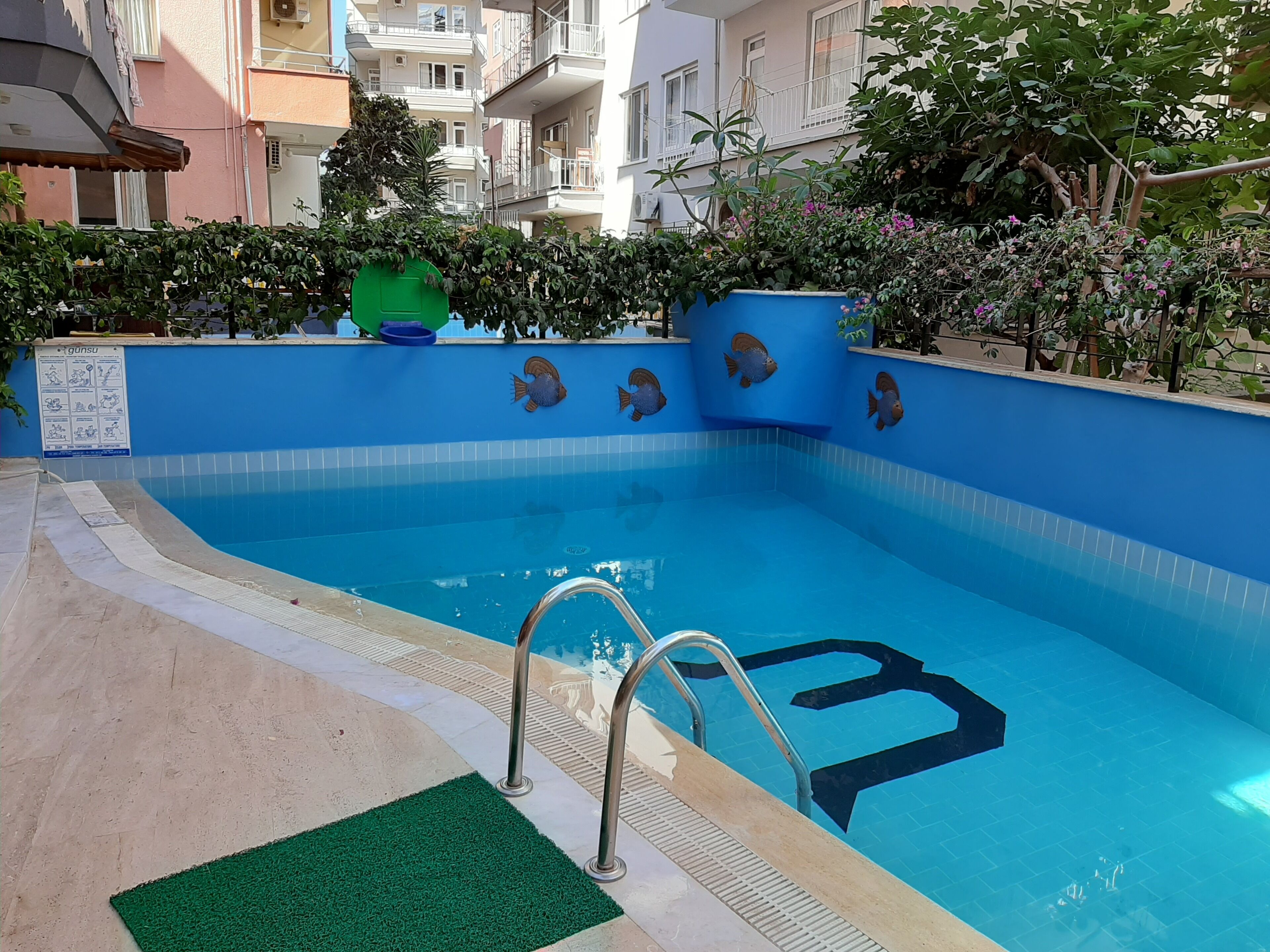 A swimming pool with a blue tiled edge, a green mat at the pool's edge, and a metal ladder leading into the water.