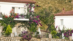 Un edificio blanco con un muro de piedra en primer plano, techo de tejas rojas y plantas en flor.