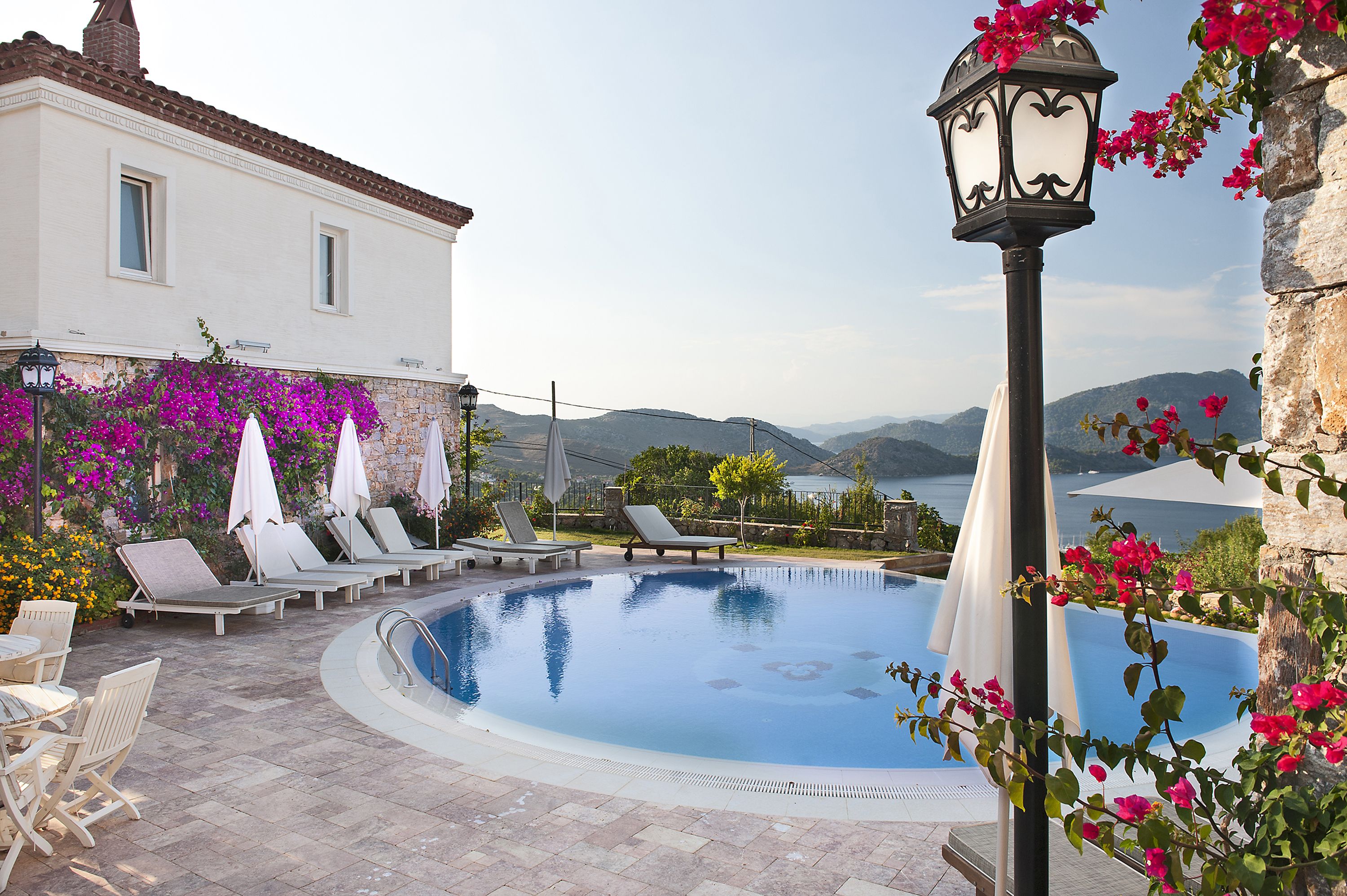 A swimming pool with lounge chairs and umbrellas, surrounded by flowers and a view of mountains.