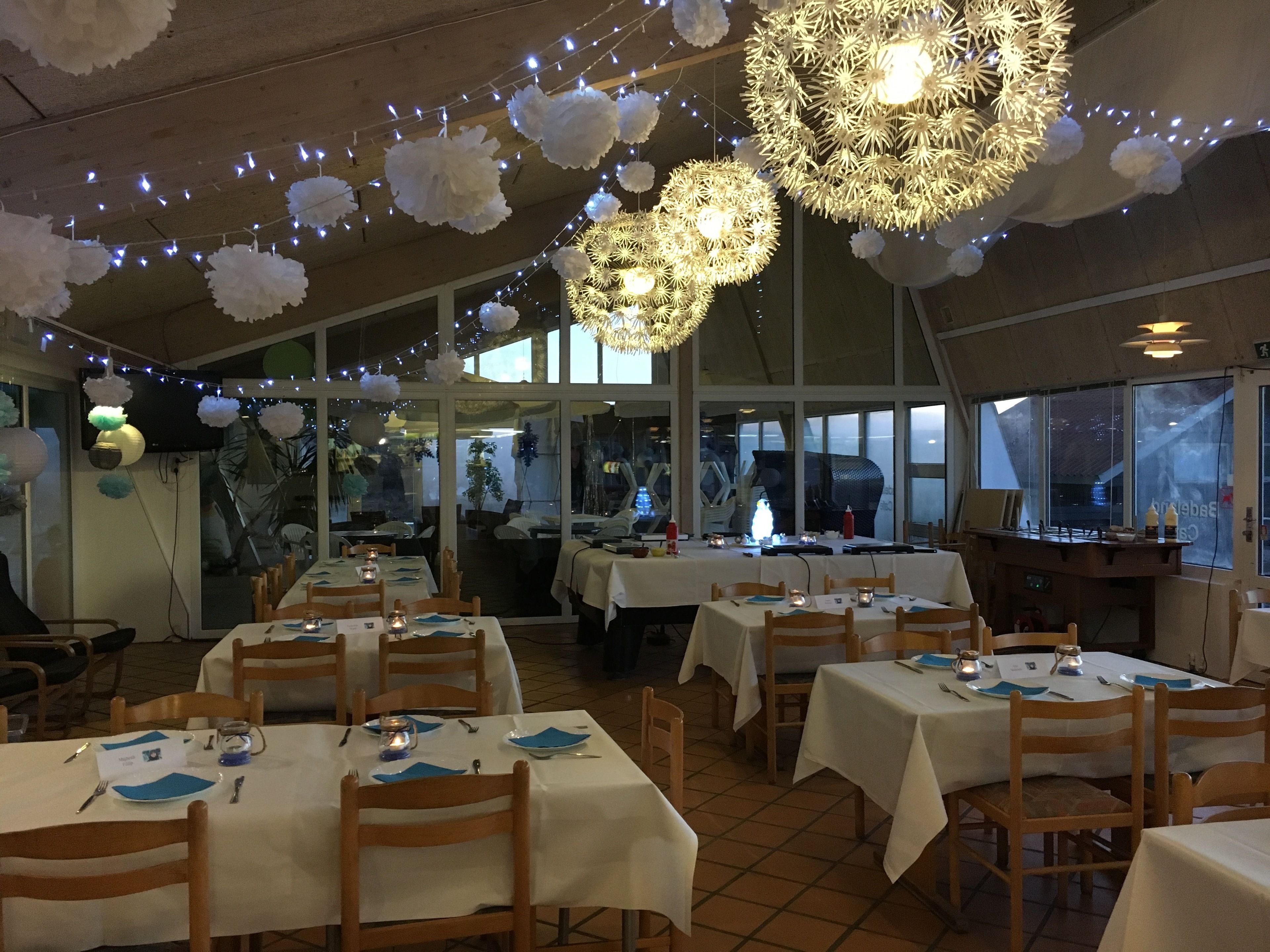 A restaurant with tables set for dining, string lights, and decorative paper flowers on the ceiling.