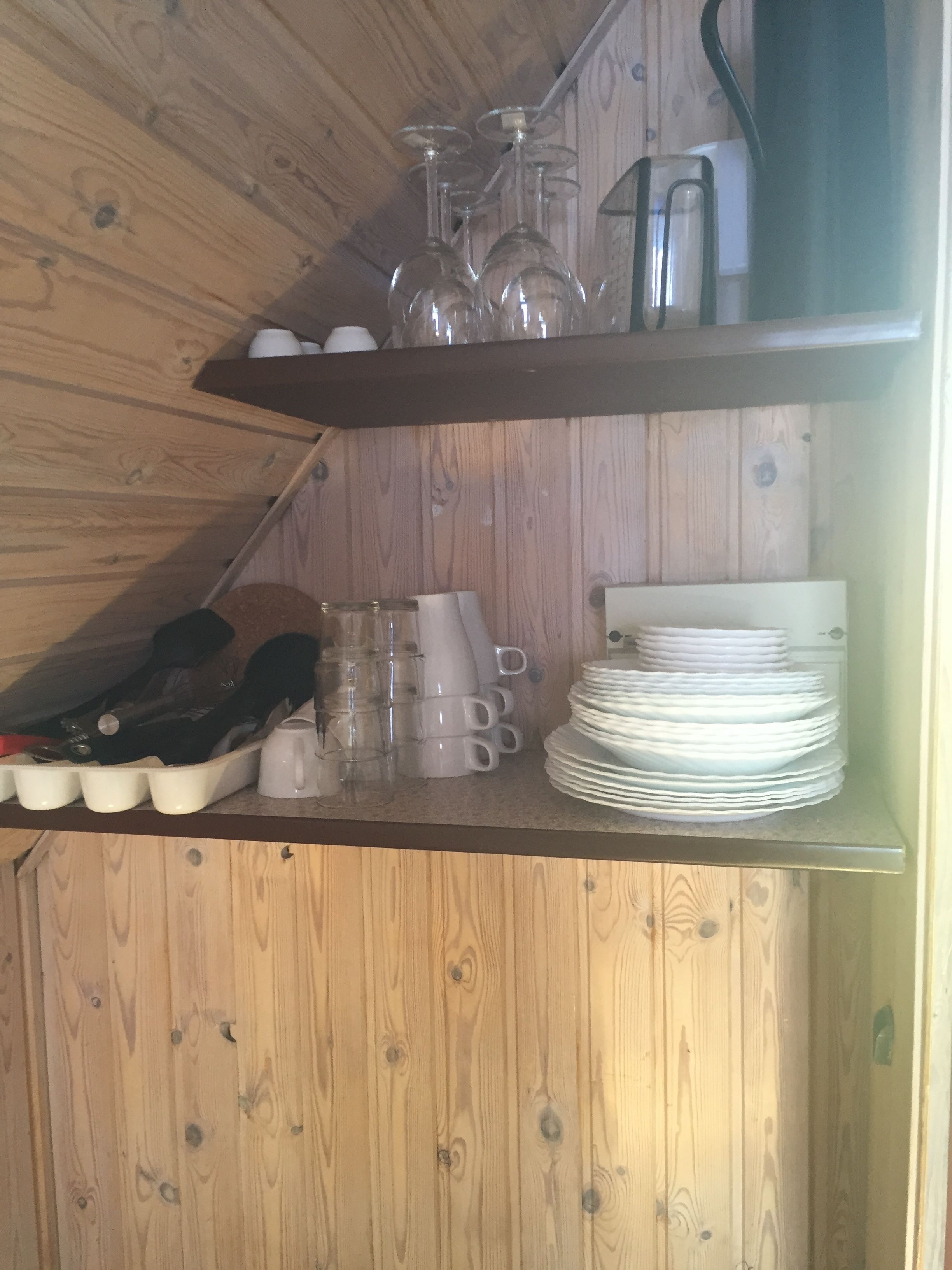 A wooden shelf with wine glasses, cups, and stacked plates.