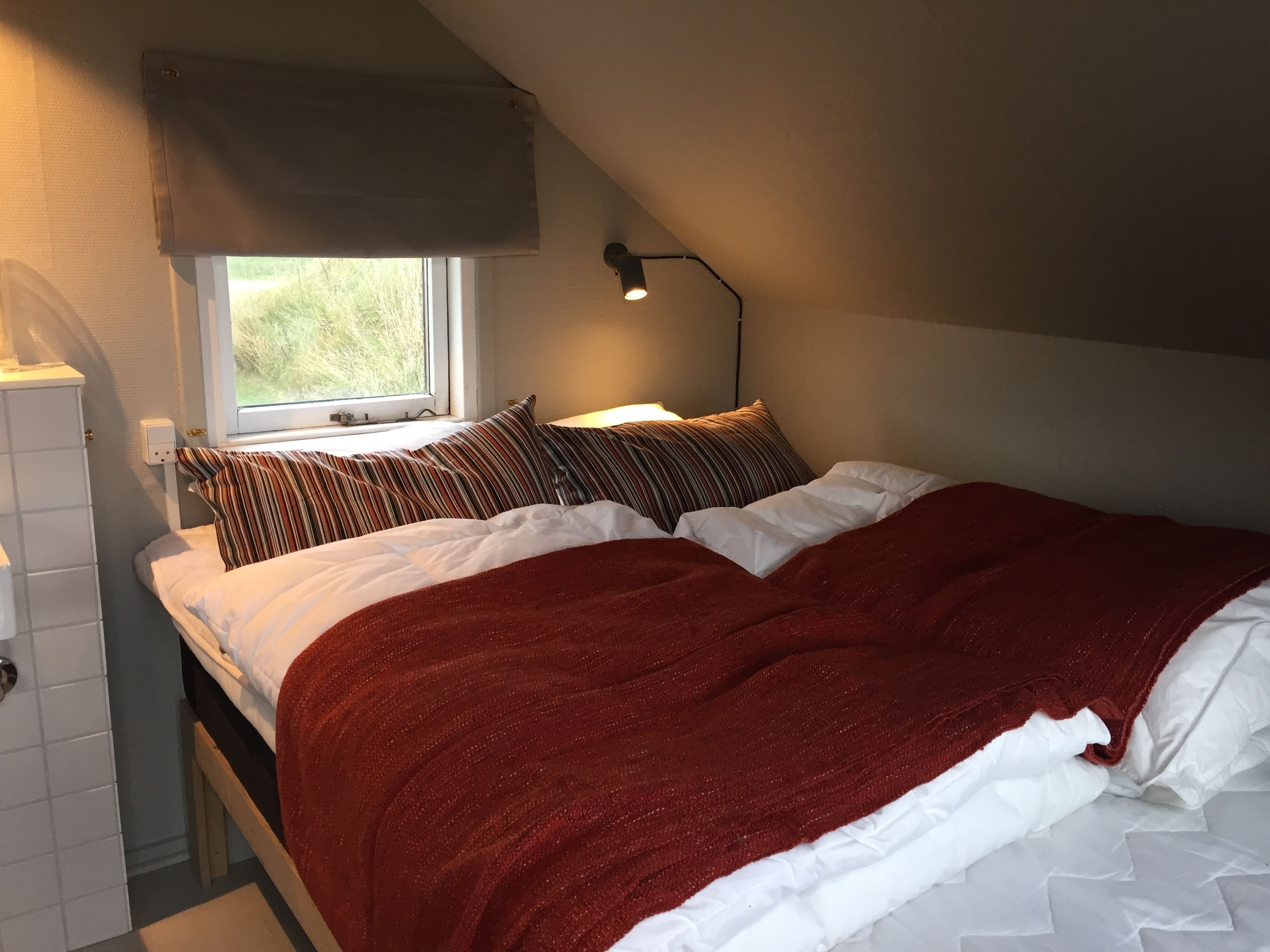 Een slaapkamer met een bed, raam, lamp en een radiator.
