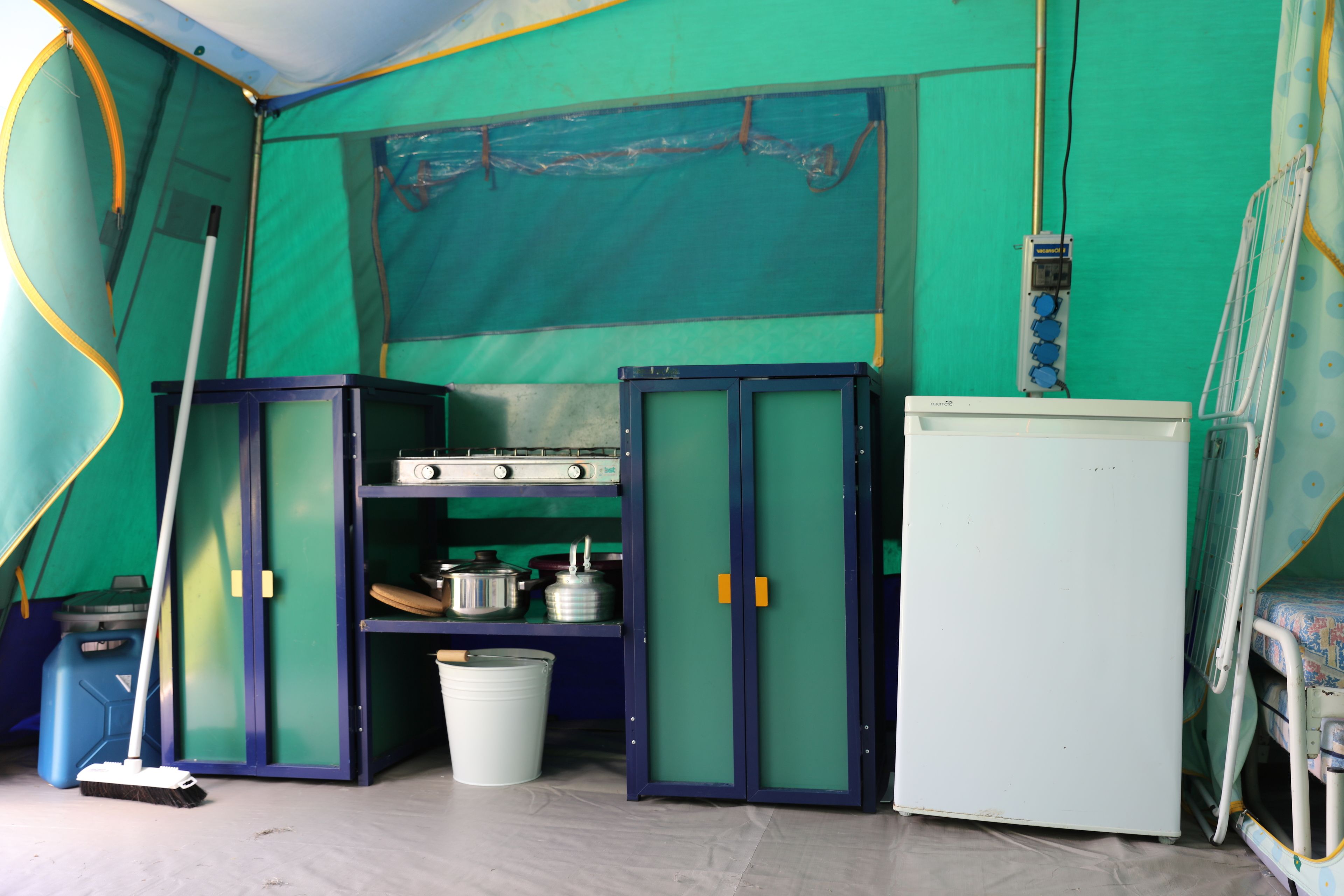 A tent with a kitchenette area including a stove, pots, and a refrigerator.