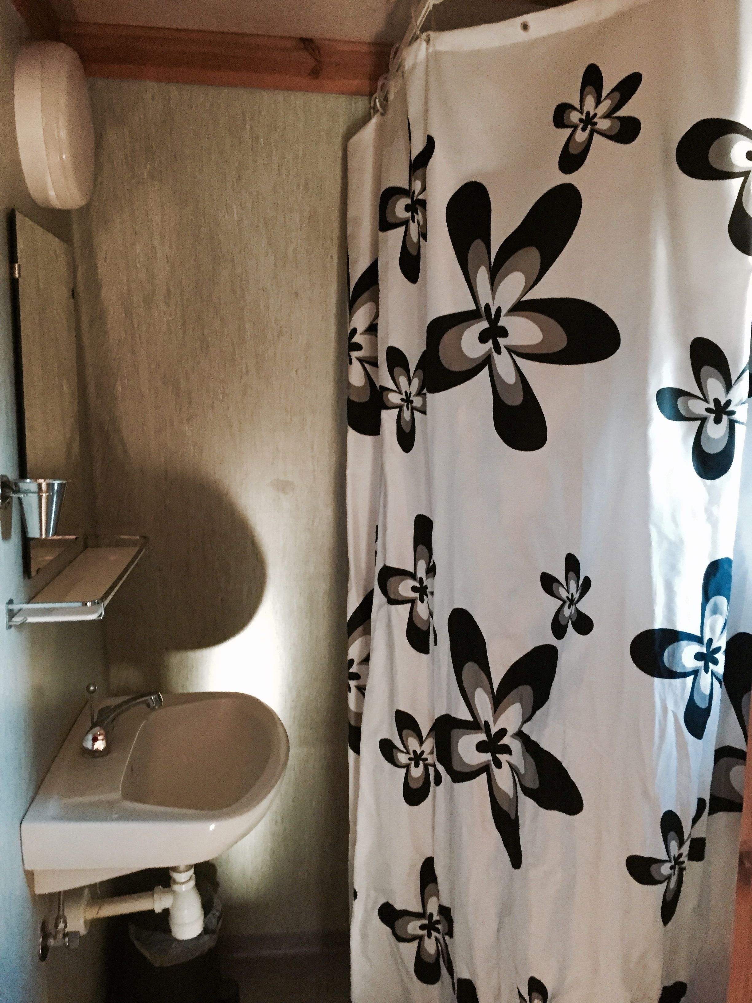 Casa de banho com cortina de chuveiro estampada com padrão floral em preto e branco, pia branca e porta-toalhas.
