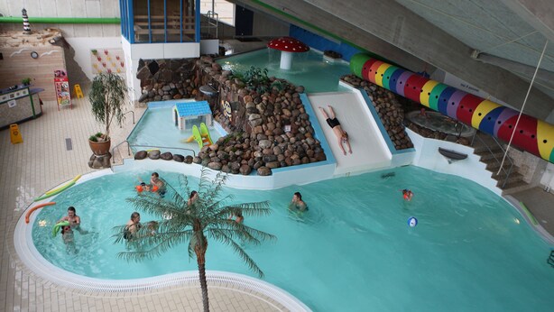 Ein Hallenbad mit mehreren Wasserrutschen und einer Felsformation.